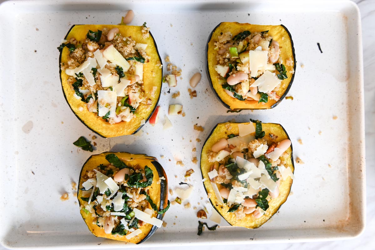 Four acorn squash halves on a white sheet pan stuffed with quinoa and Parmesan