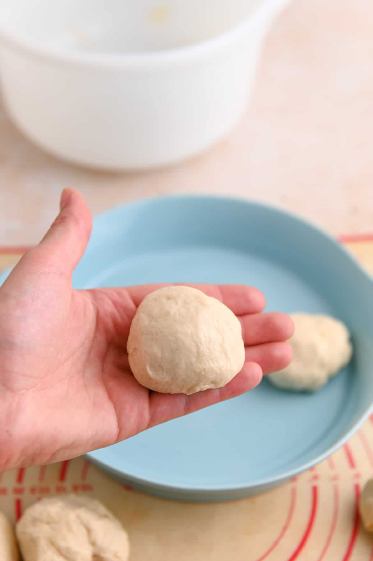 Small white dough ball in a hand in front of a blue dish