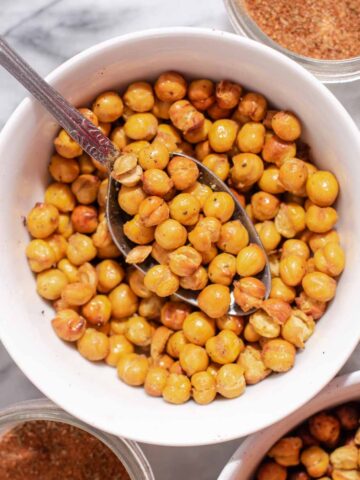 Overhead view of white bowl filled with air fryer chickpeas and metal spoon on a marble background.