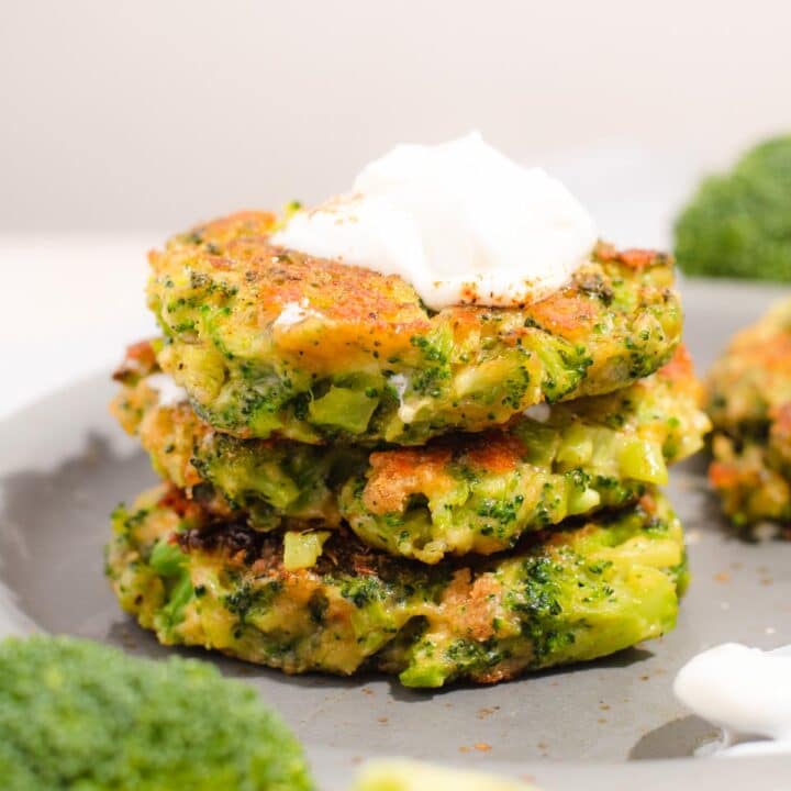 Side of a stack of three broccoli fritters with sour cream on top
