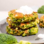 Side of a stack of three broccoli fritters with sour cream on top