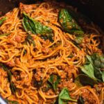 Close up of swirls of spaghetti in red sauce with pieces of green spinach