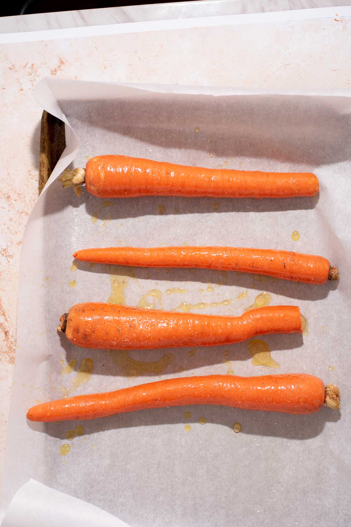 Four whole carrots on parchment paper lined baking sheet.