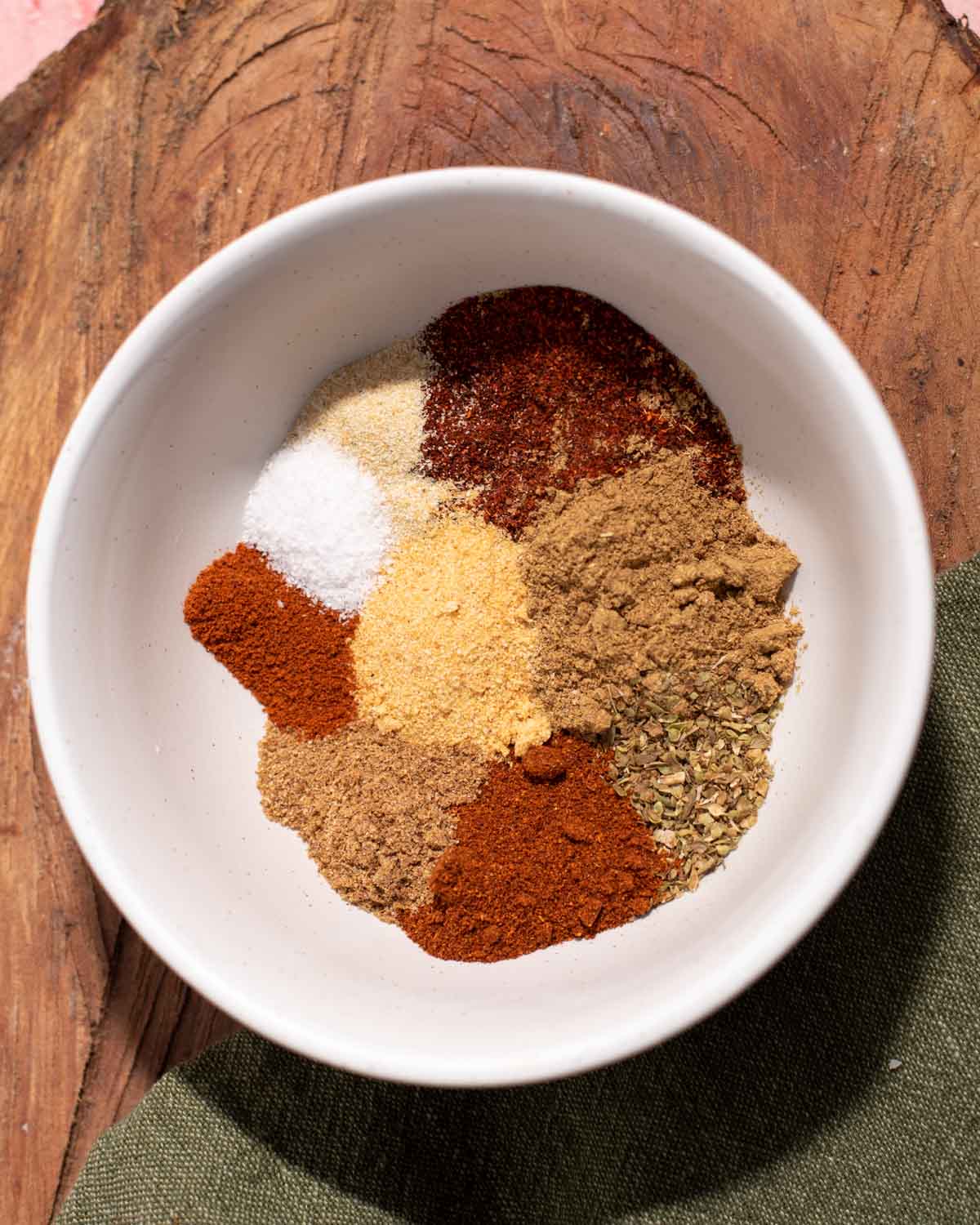 White bowl filled with variety of spices on a wooden background.