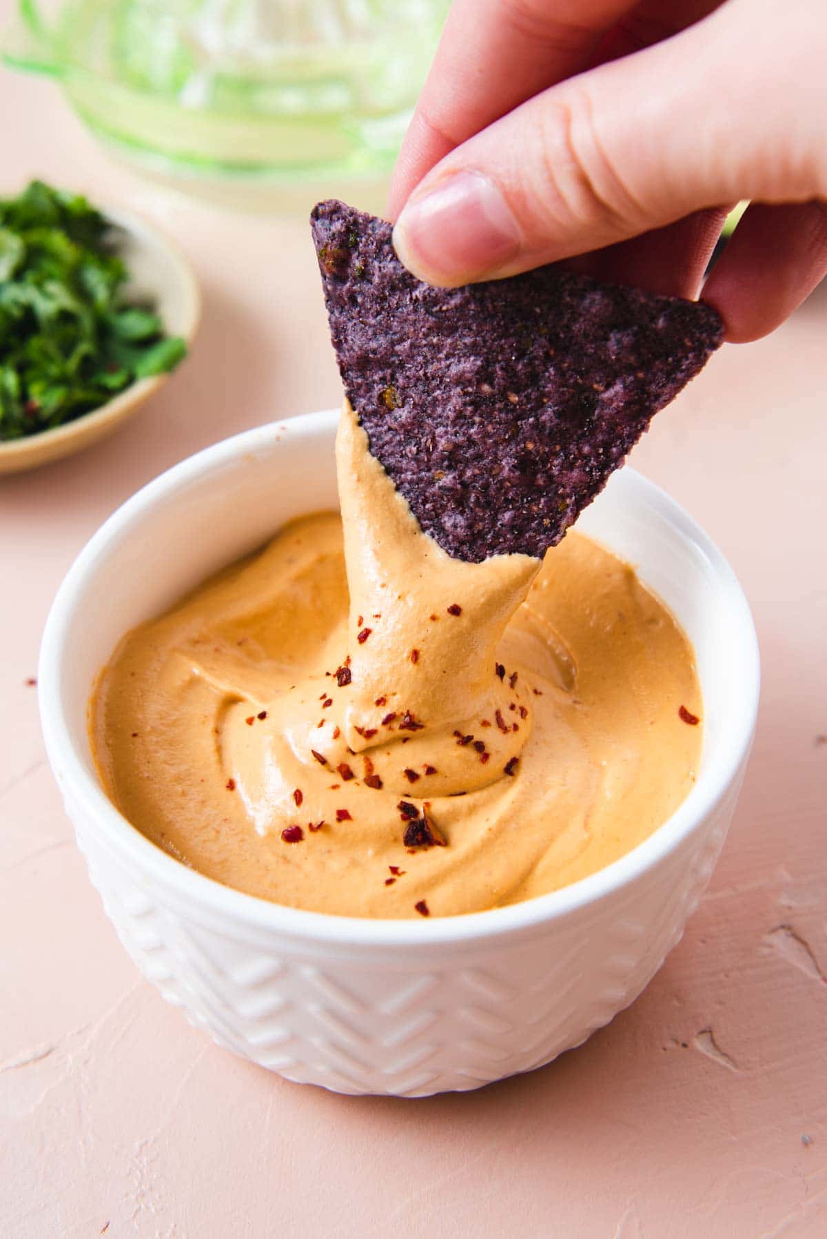 Purple tortilla chip being dipped into white bowl of cashew cheese