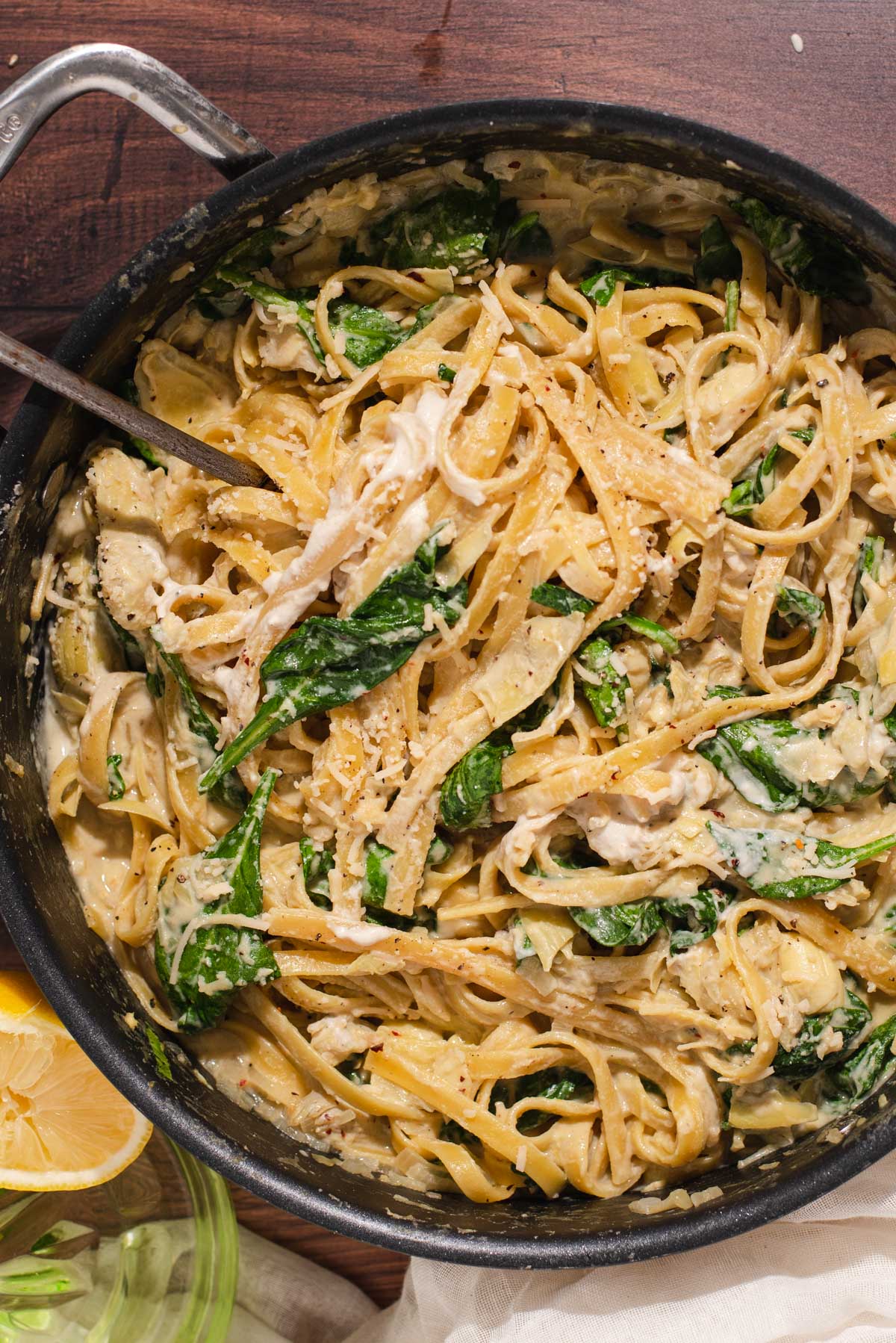 Overhead view of black skillet filled with fettuccine and wilted spinach