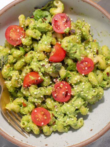 Overhead view of gray bowl filled with avocado pesto pasta and cherry tomatoes.