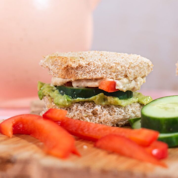 Side view of small cucumber sandwich with red bell pepper slices in front of it.