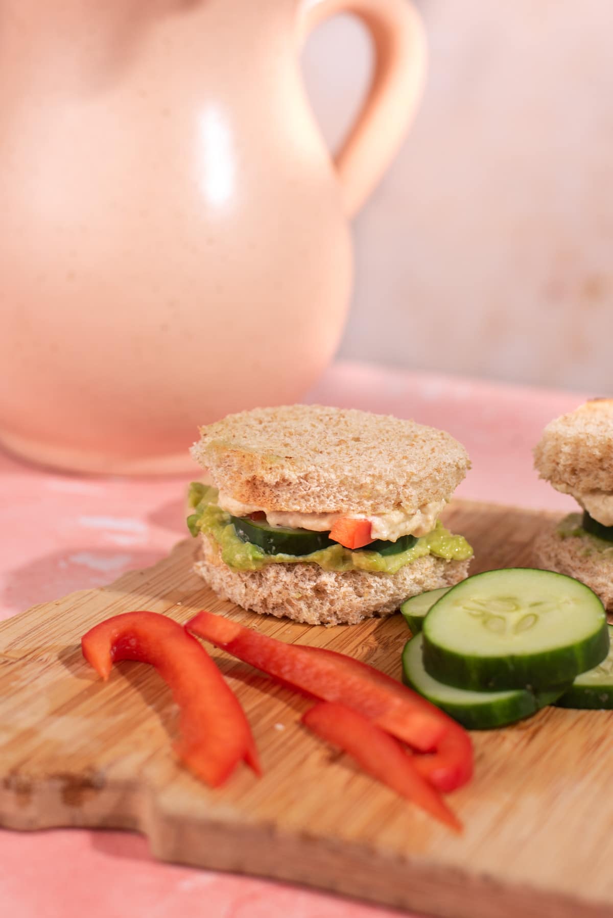 Cucumber tea sandwich on a wood cutting board with bell pepper and cucumbers.