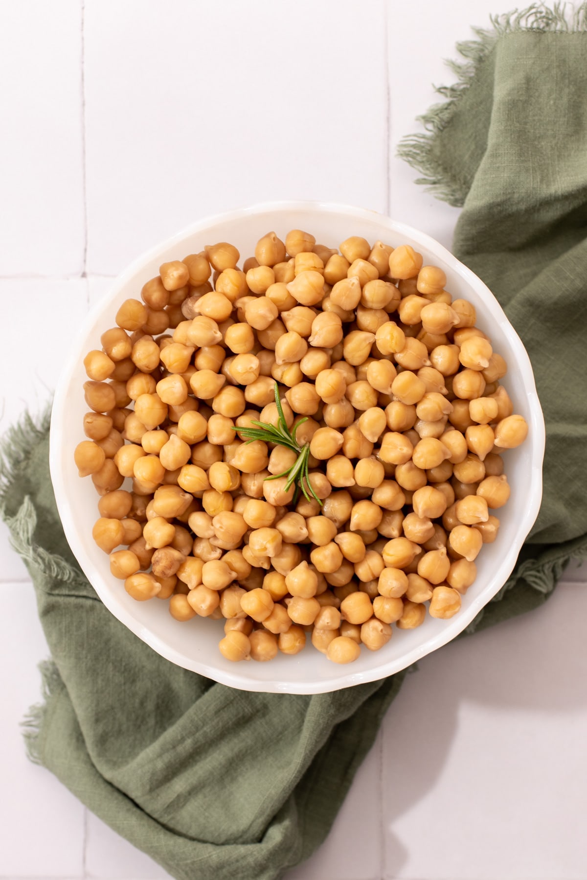 White bowl filled with Instant Pot chickpeas and a sprig of rosemary.