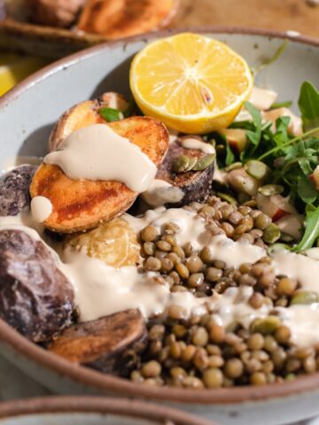 Side view of bowl of lentils and potatoes with a lemon wedge.
