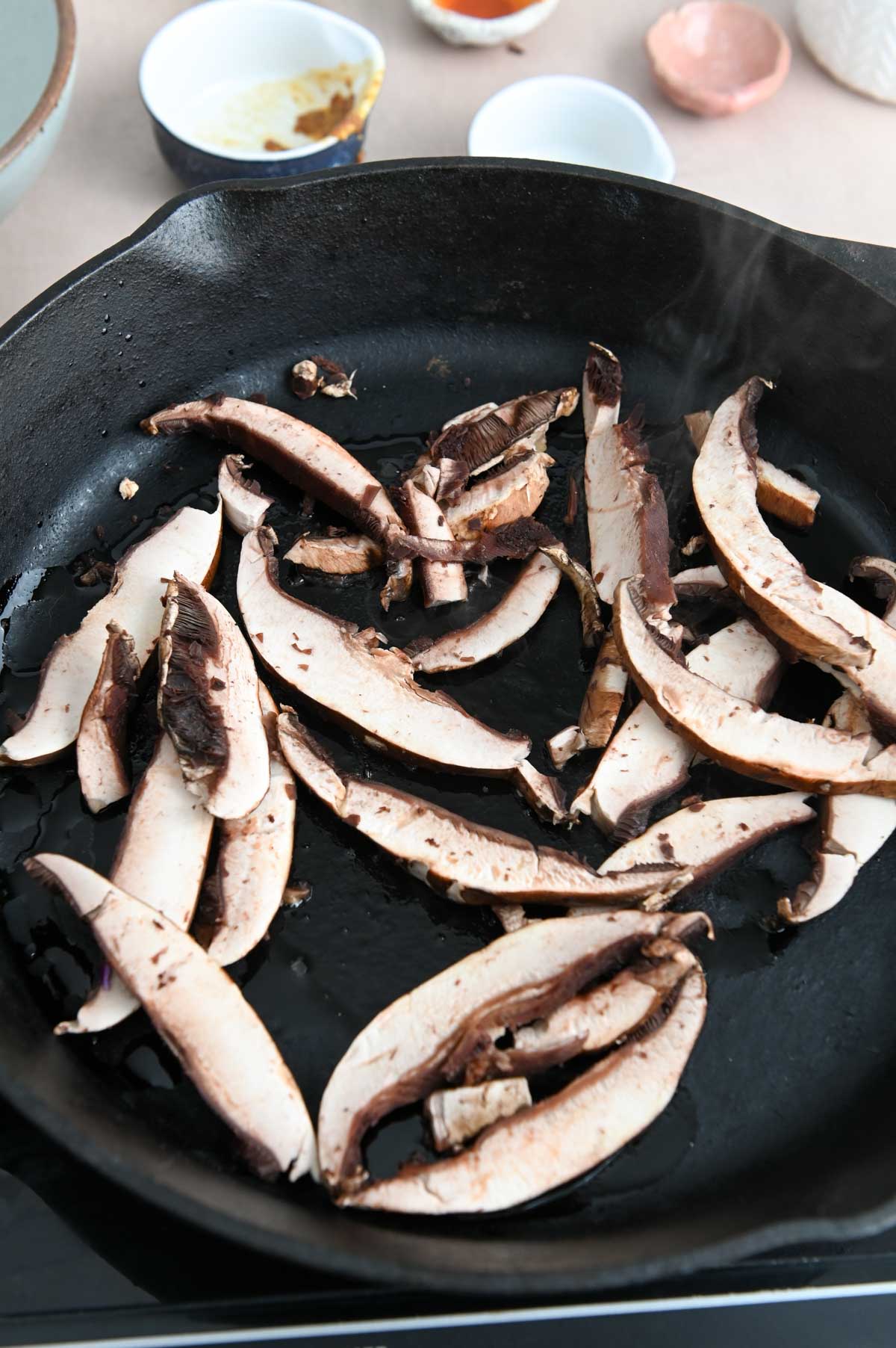 Sliced portobello mushrooms in a cast iron pan.