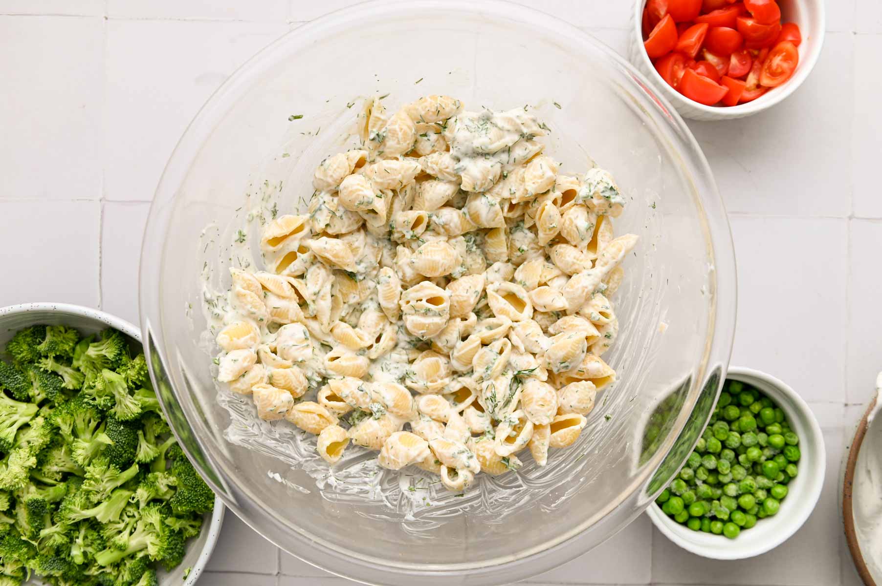 Pasta shells mixed with ranch dressing in a glass bowl.