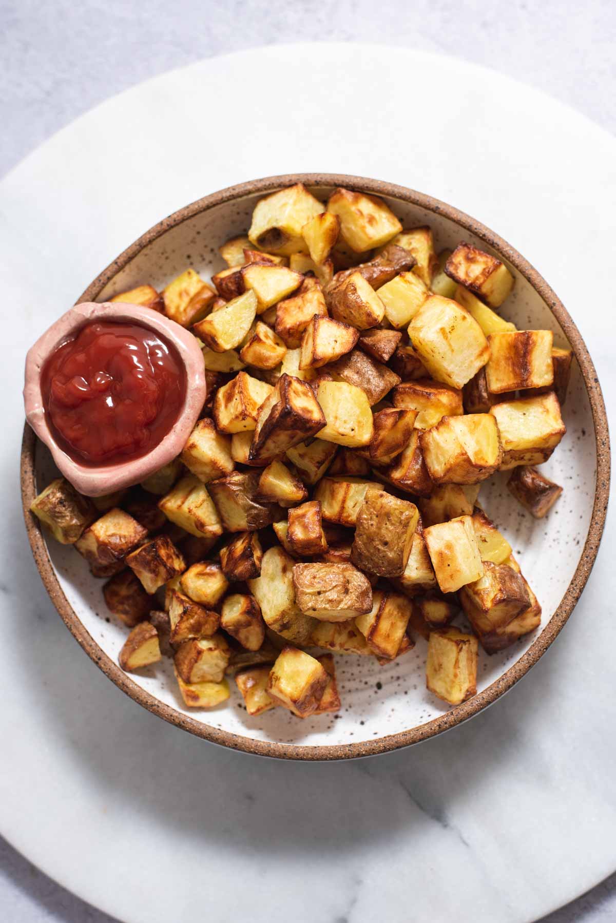 White bowl filled with air fryer roasted potatoes and a bowl of ketchup.
