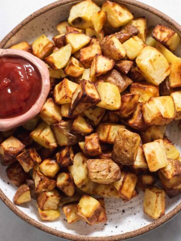 White bowl filled with roasted potatoes and a bowl of ketchup.