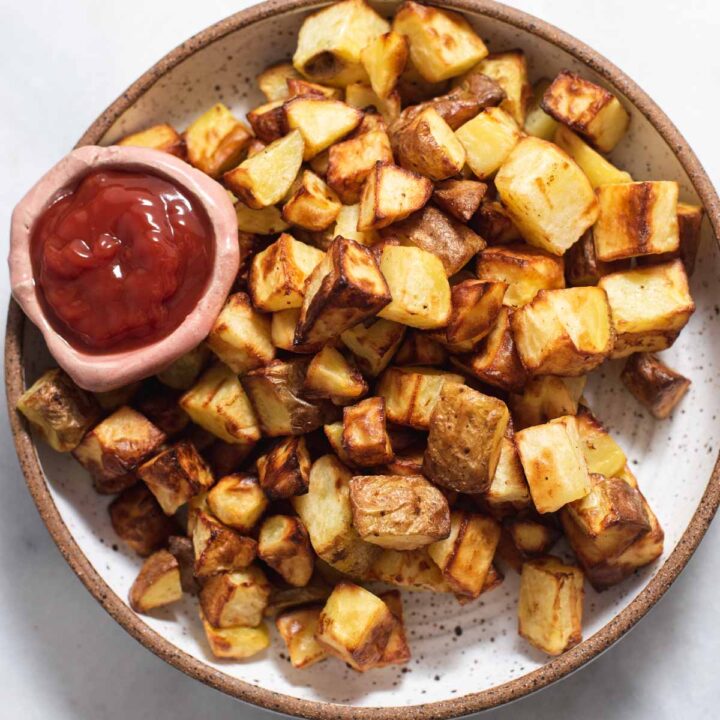 White bowl filled with roasted potatoes and a bowl of ketchup.