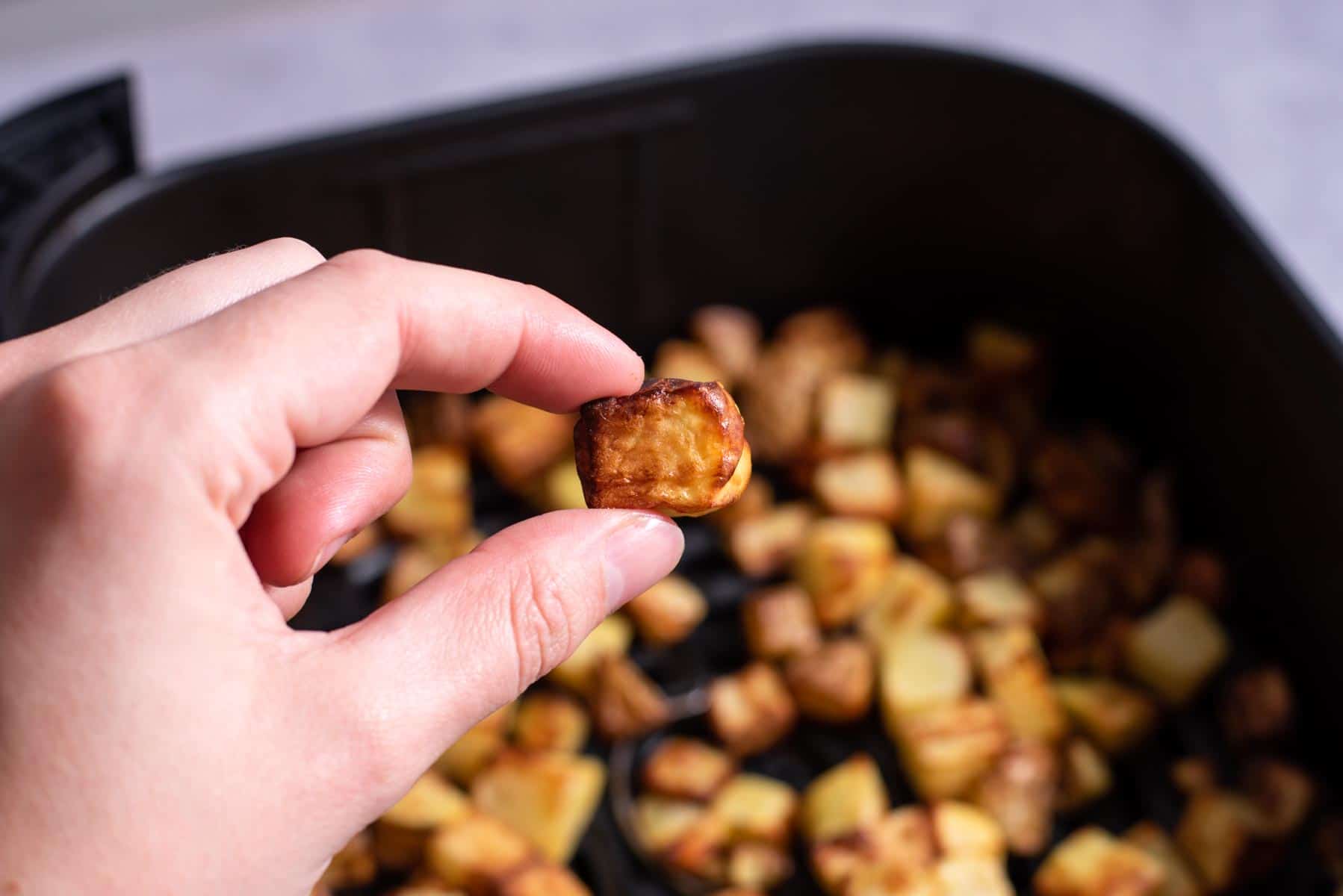 Fingers pinching one roasted potato.