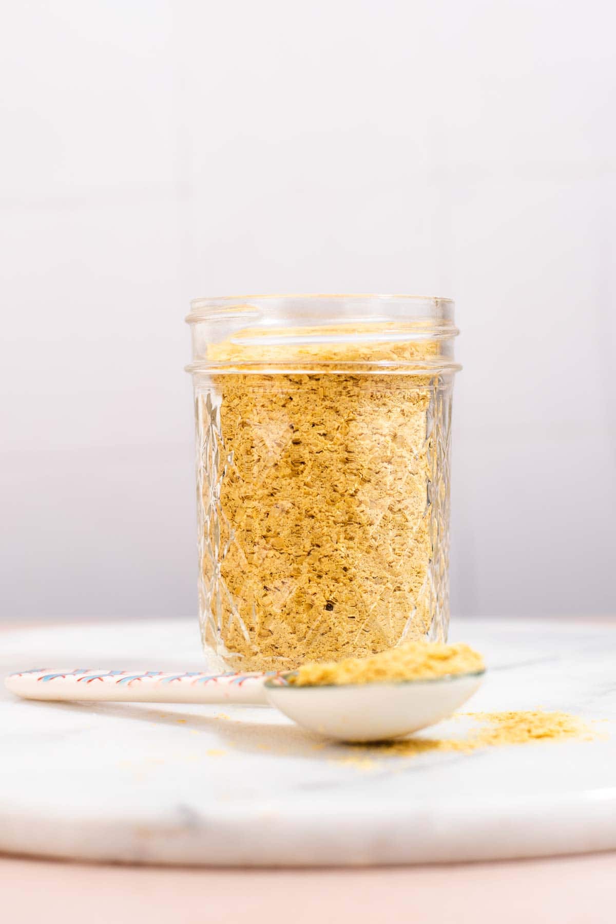 Glass jar filled with nutritional yeast in front of a gray background.
