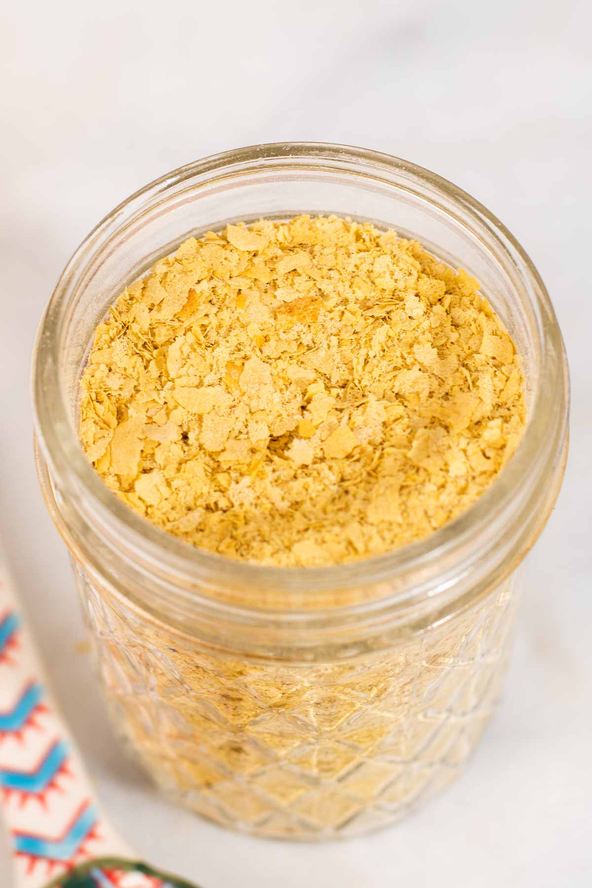 Close up of yellow nutritional yeast in a glass jar.