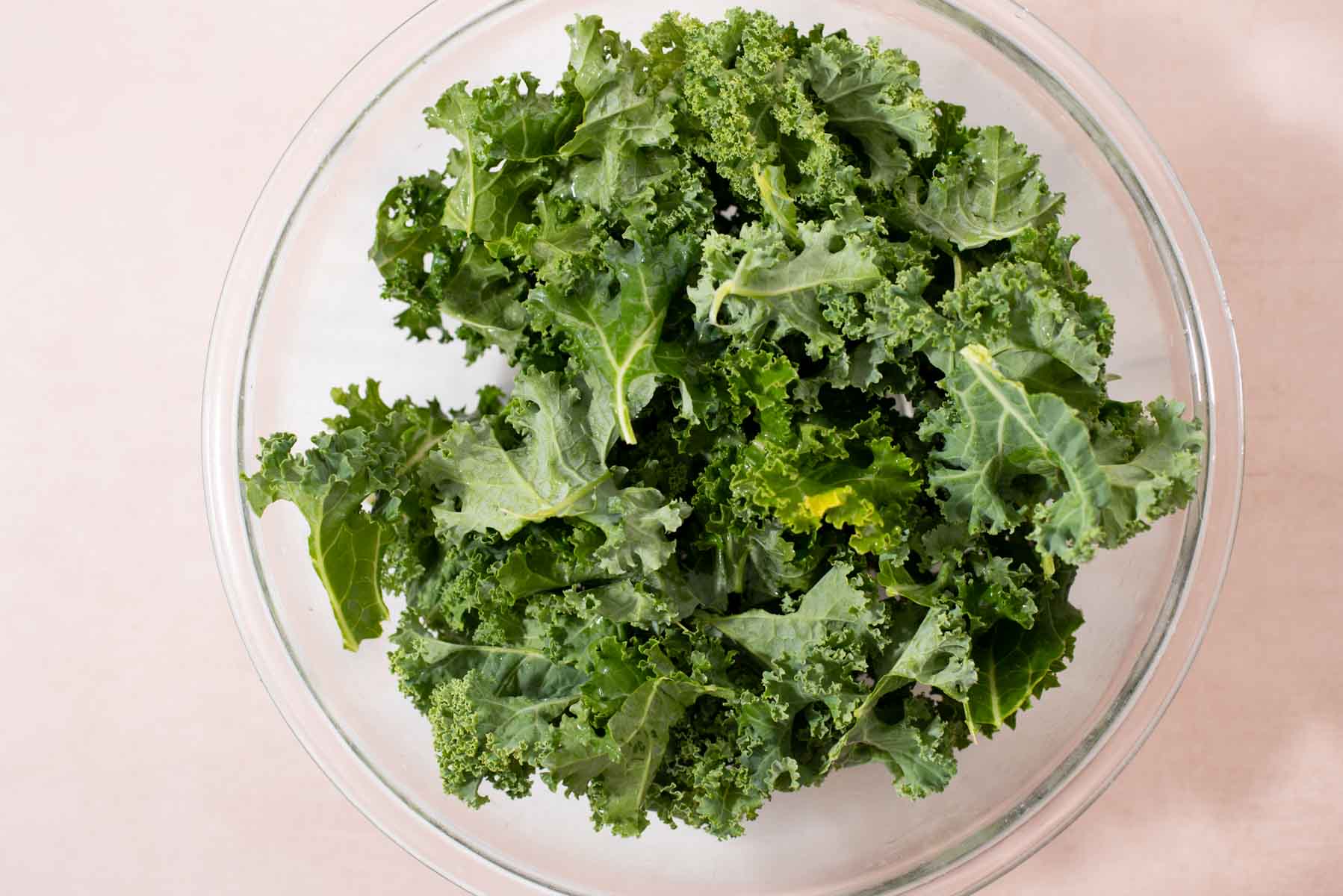 Raw kale pieces in a glass bowl.