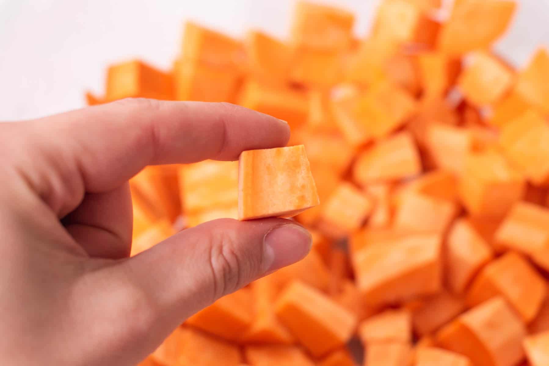 Close up of fingers holding one piece of diced sweet potato.