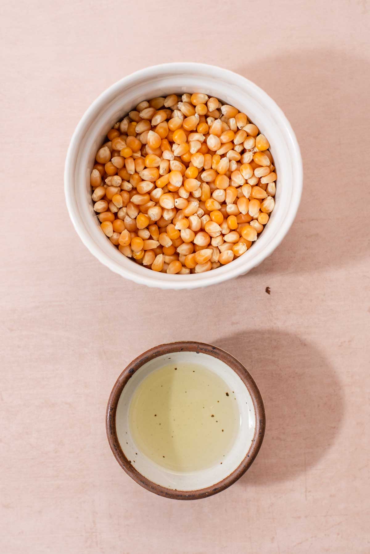 White jar of popcorn kernels and bowl of oil.