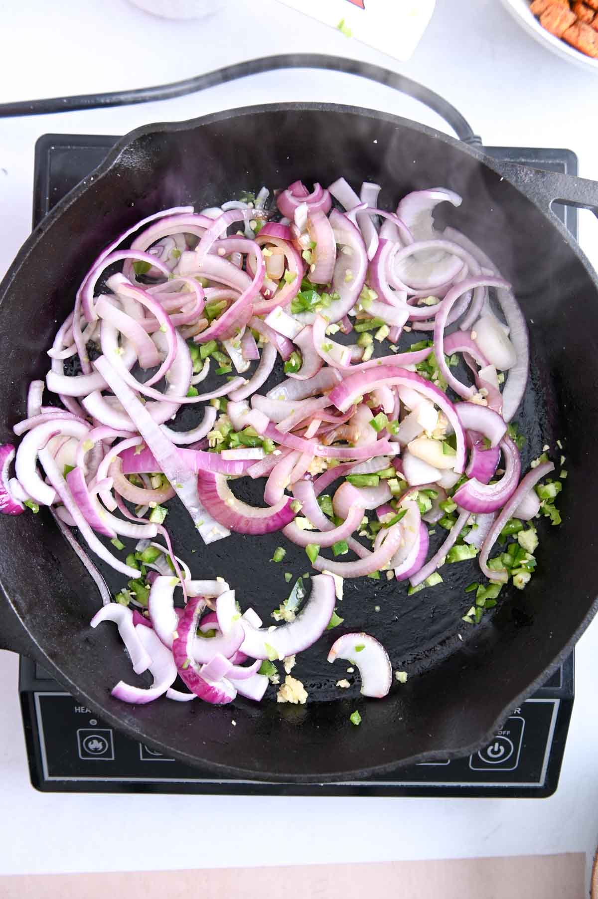 Sliced red onion and jalapeno in a cast iron skillet.