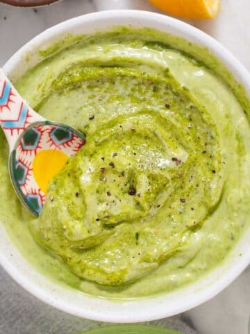 Overhead view of white bowl filled with green pesto aioli.