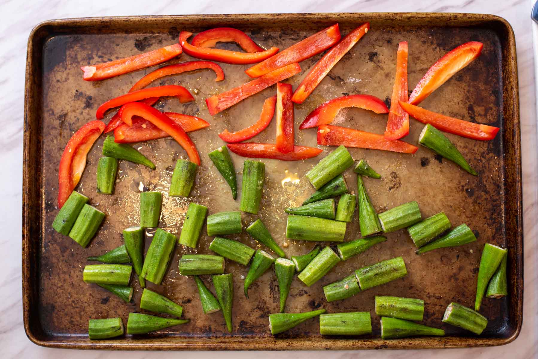 Red bell pepper strips and sliced okra on a sheet pan.