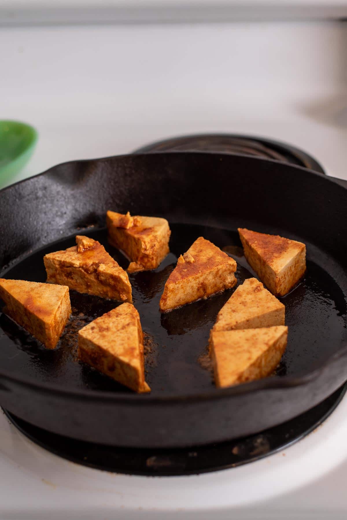 Triangles of tofu cooking in a cast iron pan.