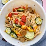 White bowl filled with zucchini, tomatoes, sausage, and fettuccine.