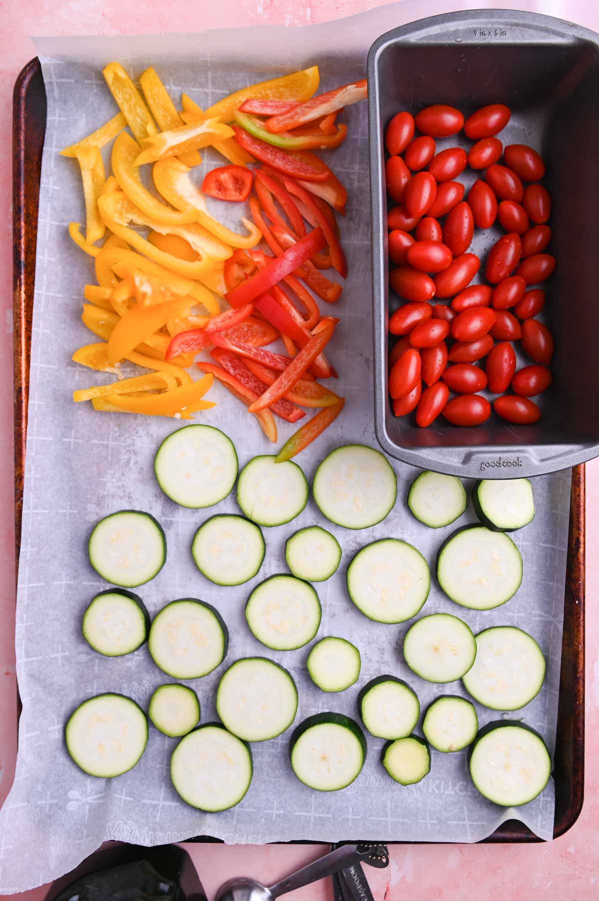 Uncooked zucchini, bell pepper, and tomatoes on a sheet pan.