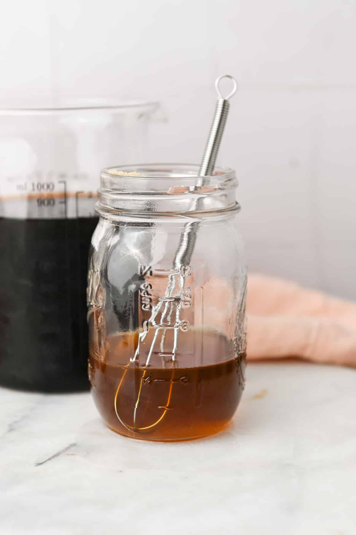 Pint sized jar with brown sugar simple syrup and a small whisk inside.