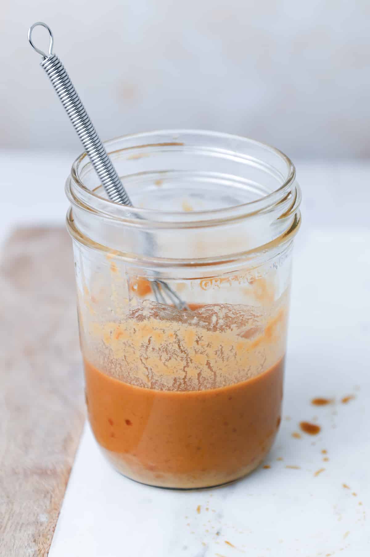 Peanut sauce in a glass jar with a small whisk.