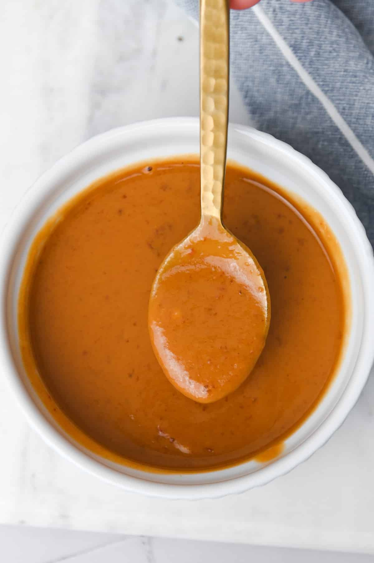 Gold spoon with peanut butter in a white ramekin of peanut sauce.