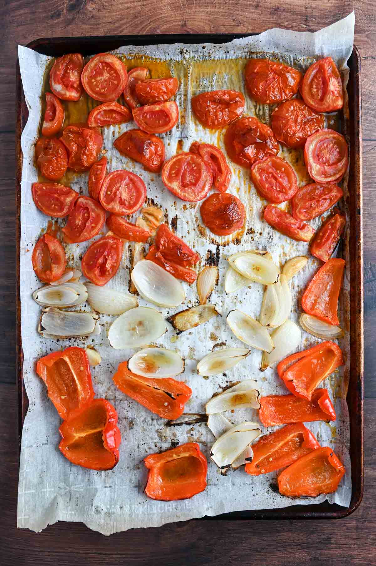 Roasted tomatoes, onions, and peppers on a sheet pan.