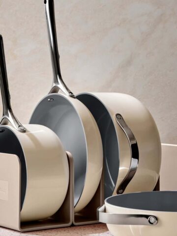 Cream colored caraway cookware set in a metal divider in front of a cream wall.