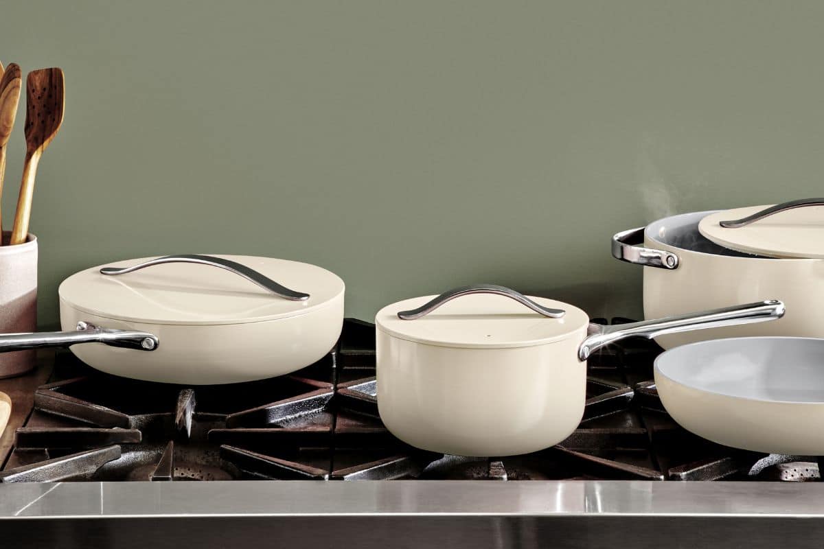 Four pieces of cream Caraway cookware on a stainless steel stove.