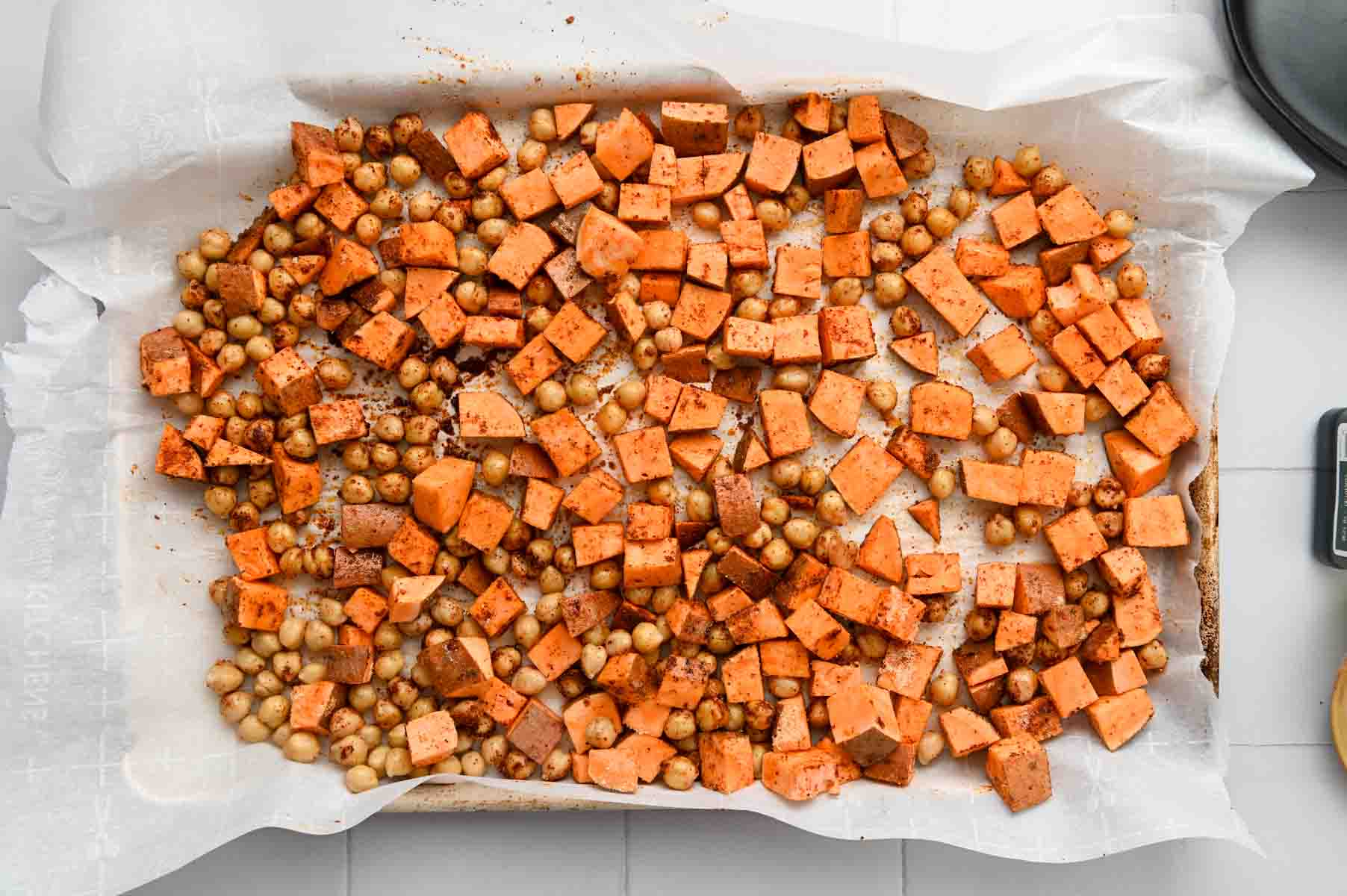 Cubed sweet potato and quinoa on a parhcment paper lined baking sheet.