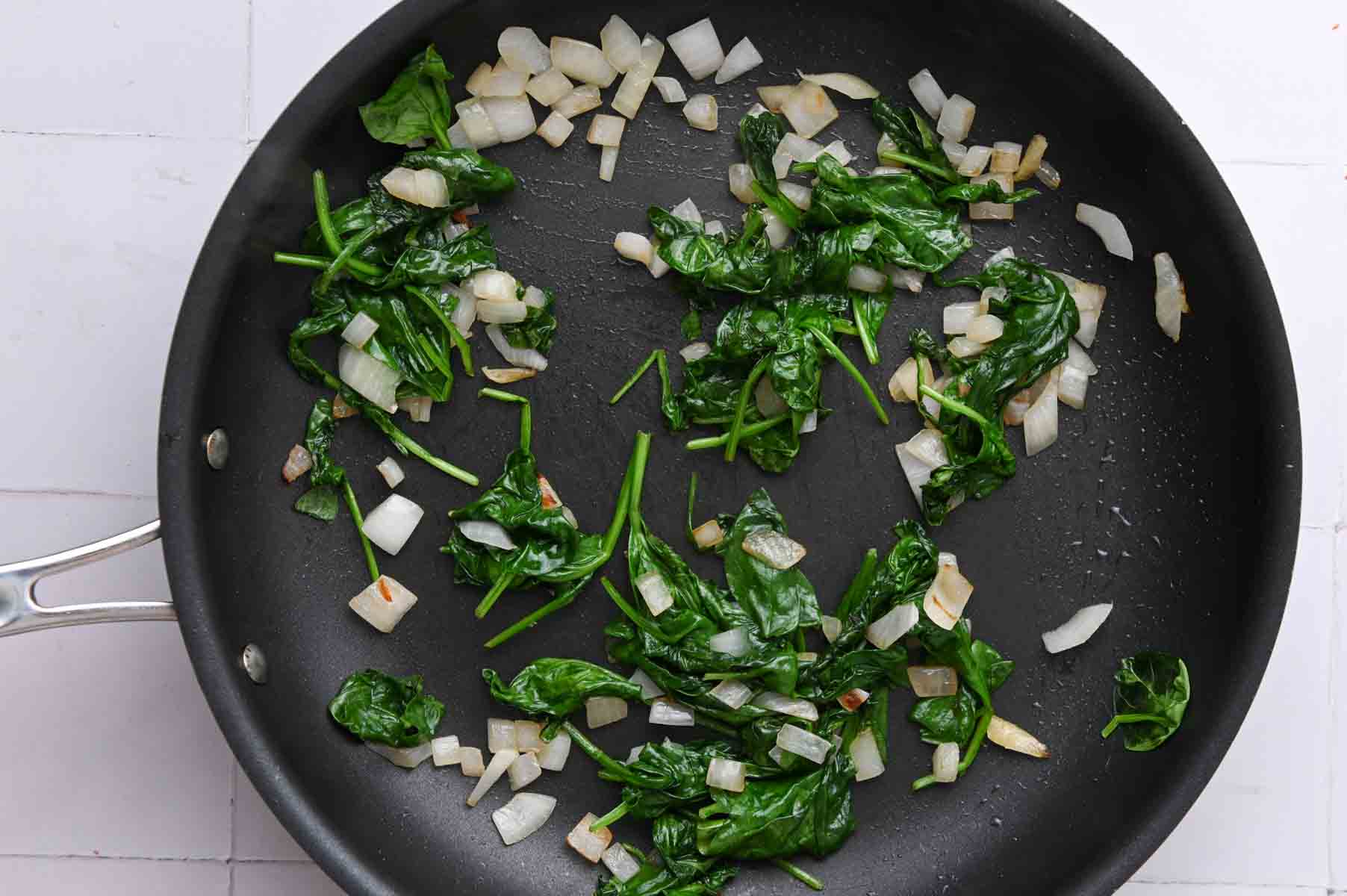 Wilted spinach and onion in a black pan.