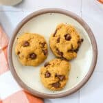Three pumpkin cookies on white plate with a brown trim.