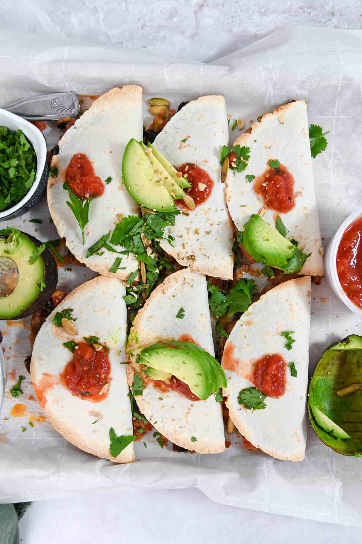 Overhead view of six baked tacos topped with avocado slices and salsa.