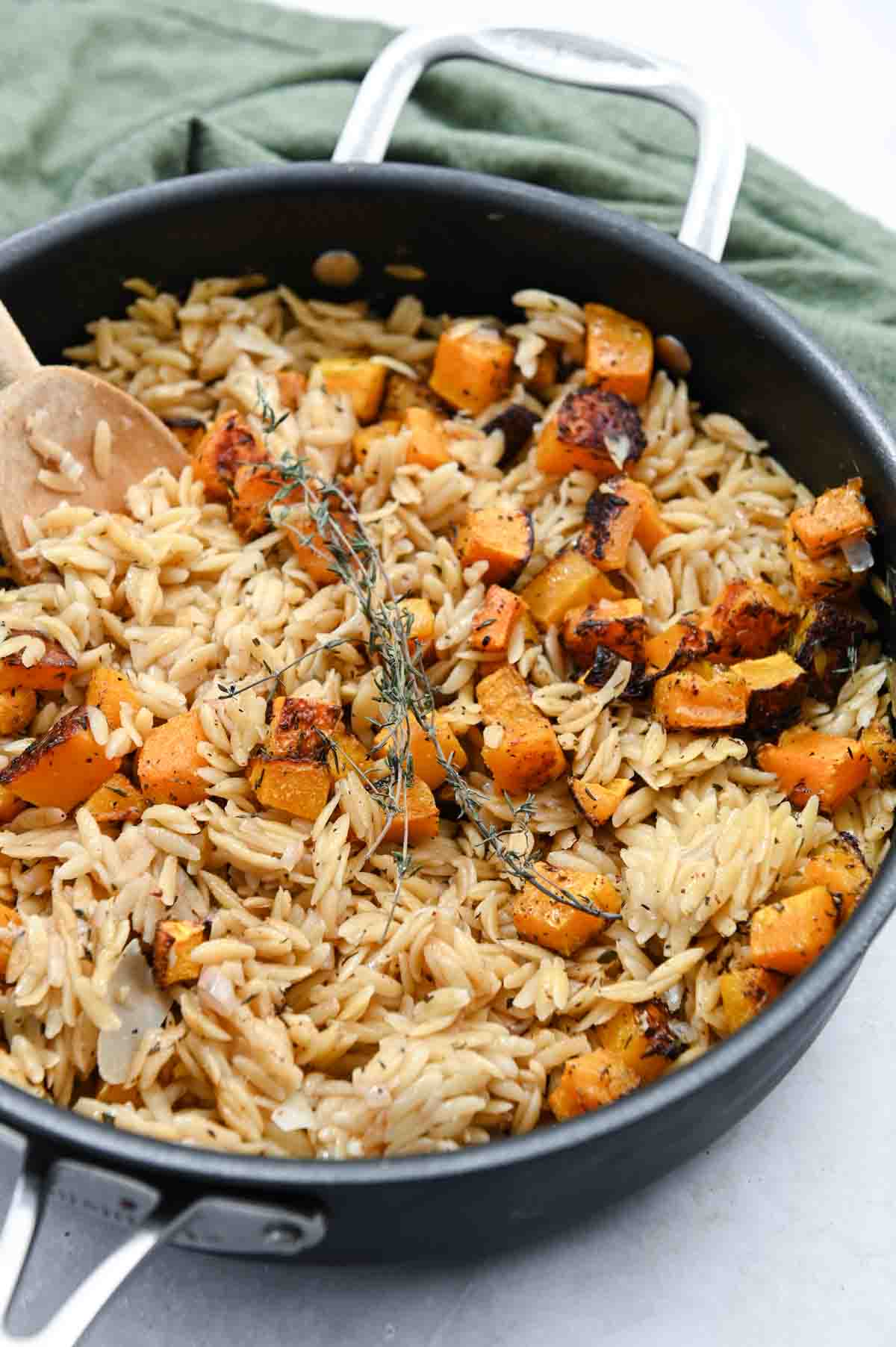 Close up of orzo with butternut squash and a wooden spoon in a skillet.