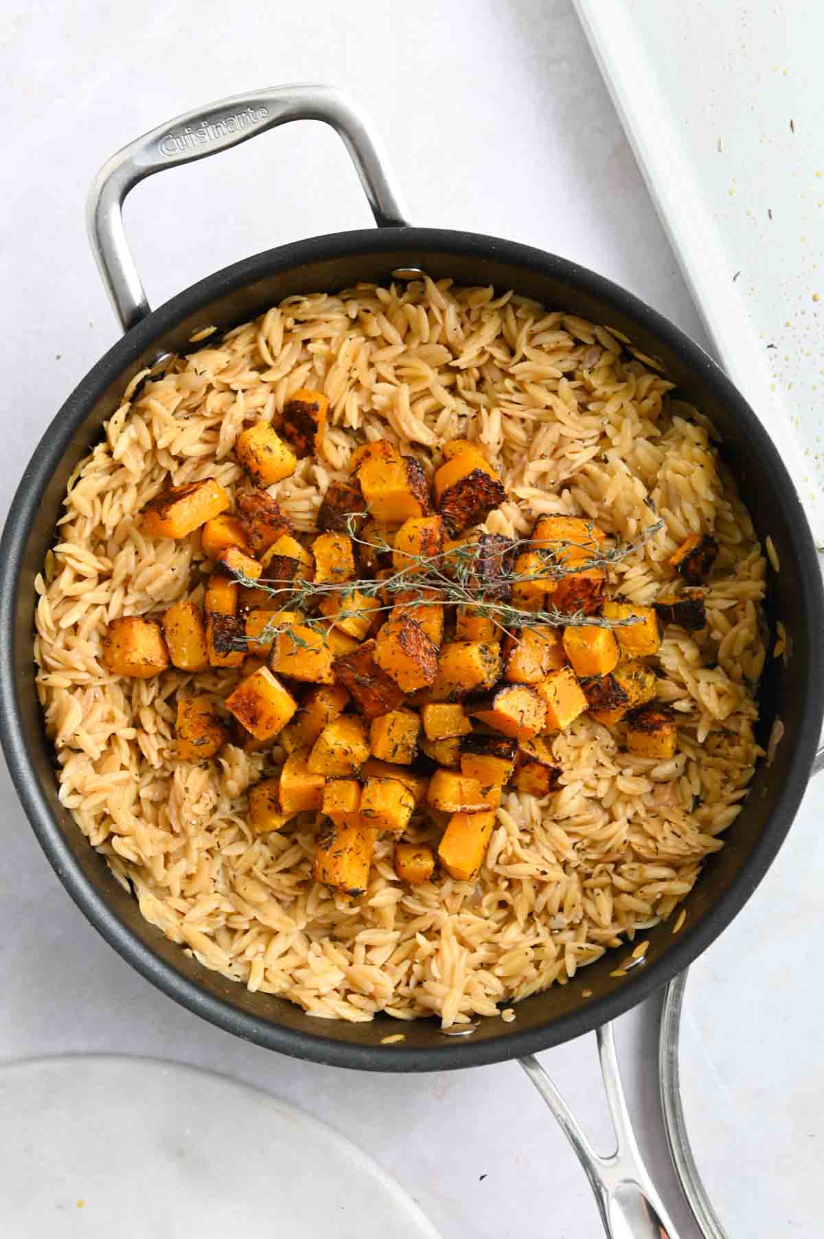 Orzo in a black skillet topped with roasted butternut squash on a white background.