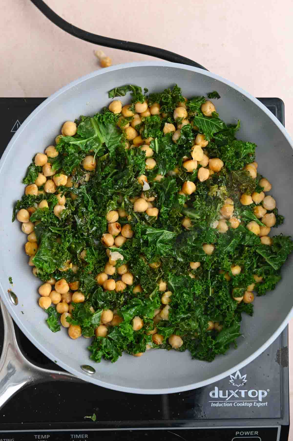 Wilted green kale with chickpeas in a gray skillet.