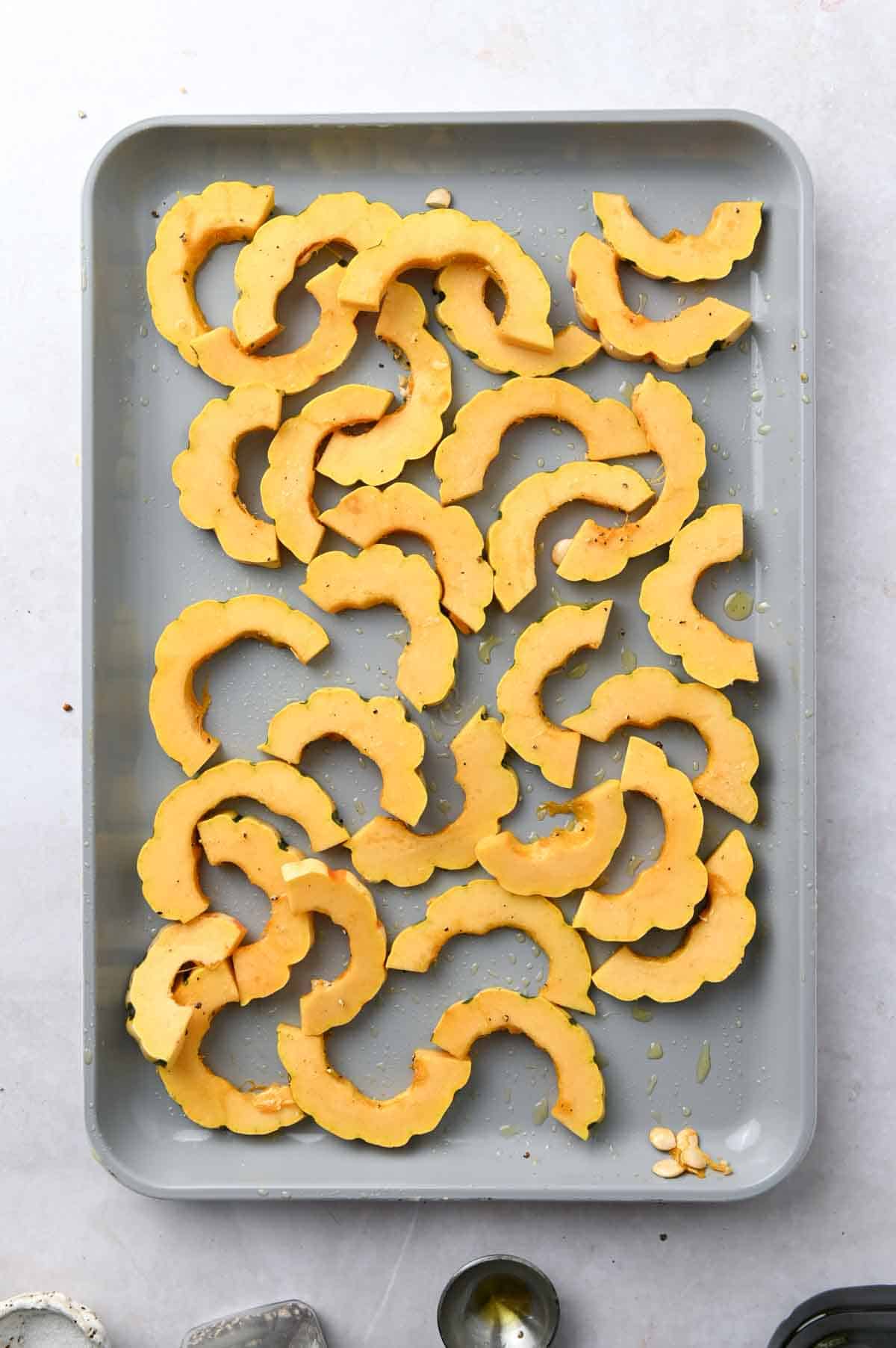 Sliced and uncooked delicata squash on a baking sheet.
