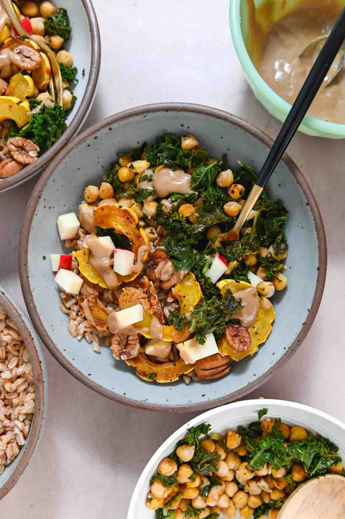 Gray bowl filled with farro, delicata squash, and other grain bowl ingredients with a black handled gold fork.