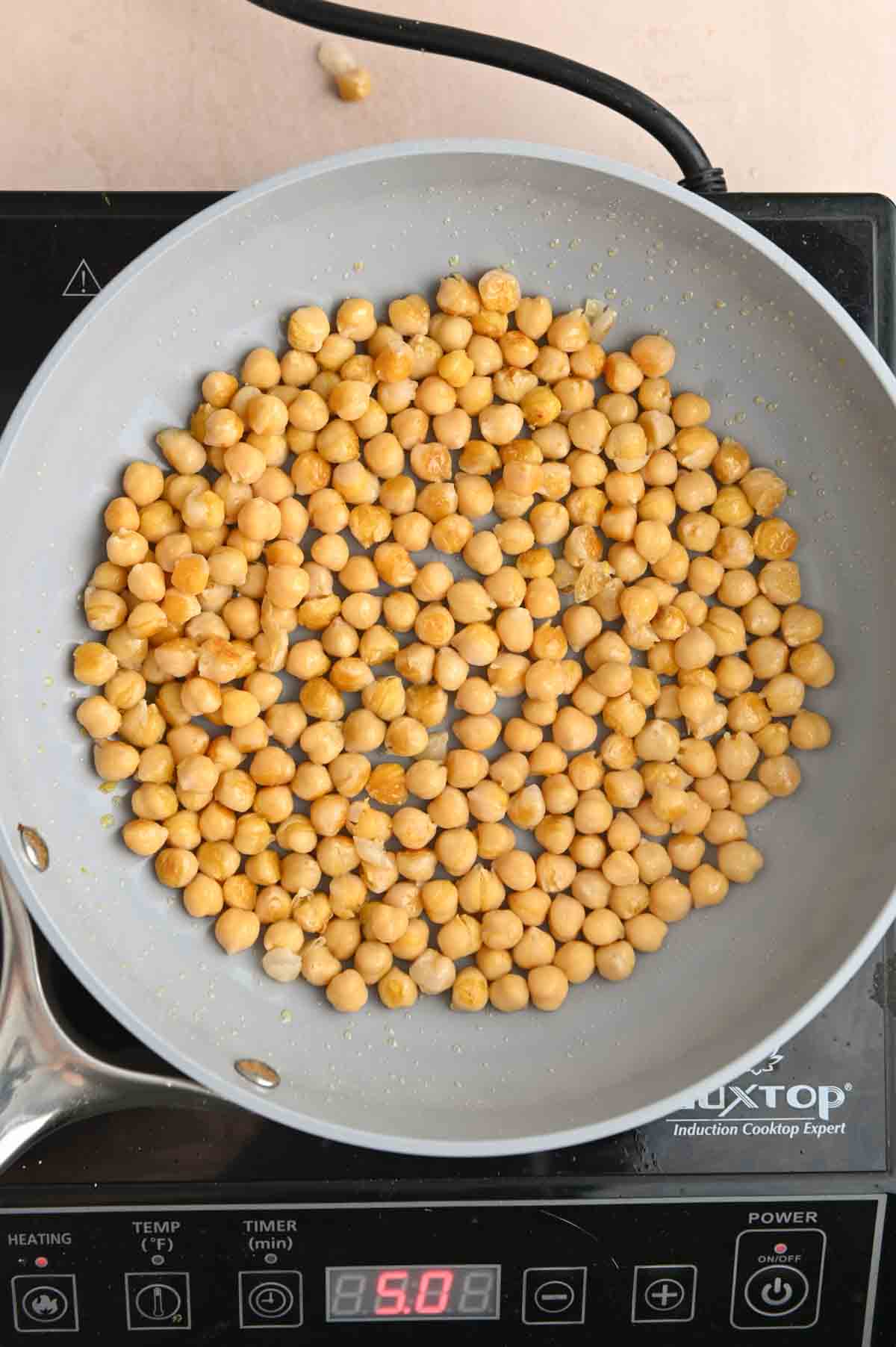 Chickpeas cooking in a gray skillet on a black cooktop.
