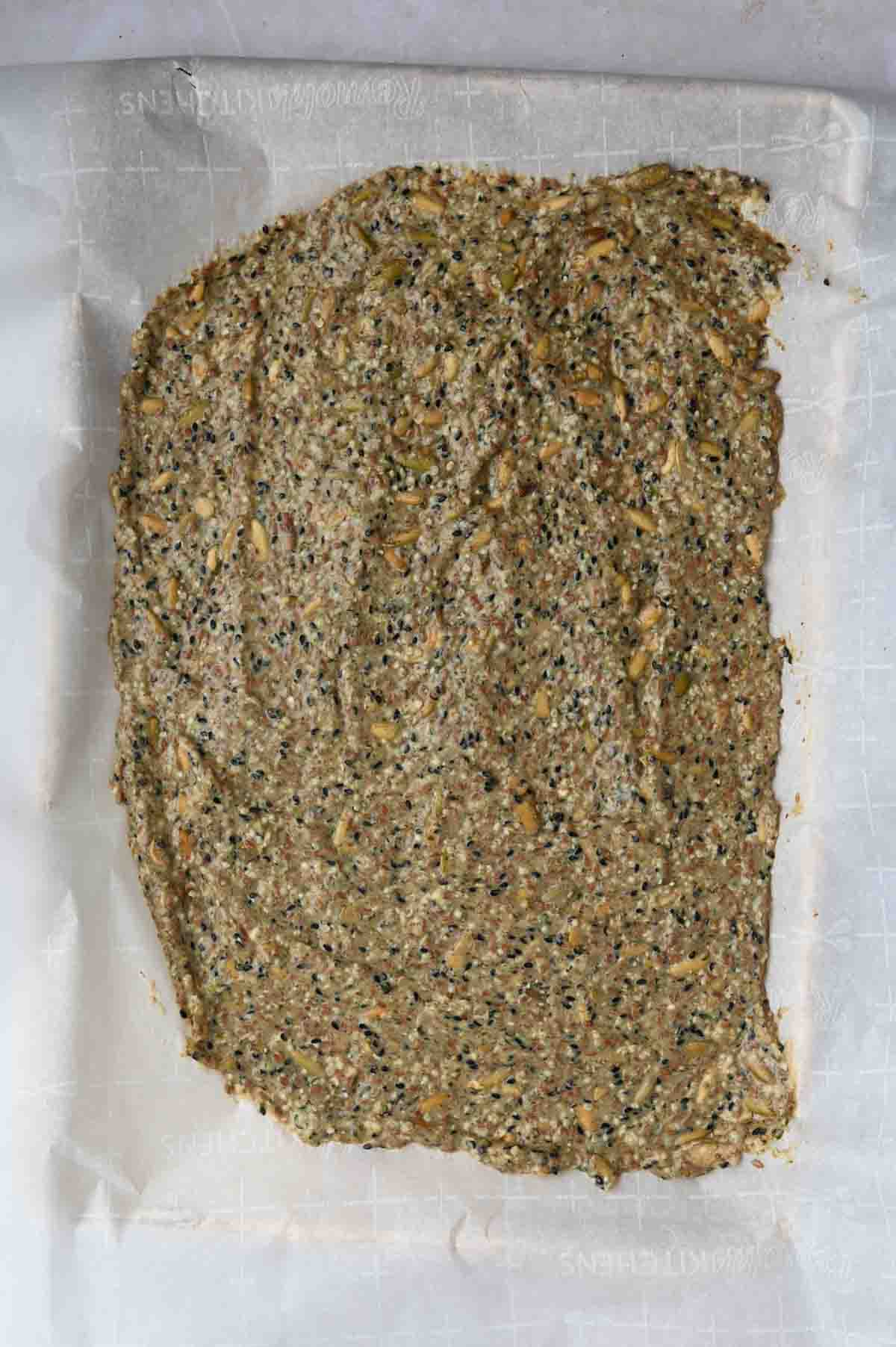 Cracker dough flattened out onto a parchment paper baking sheet.