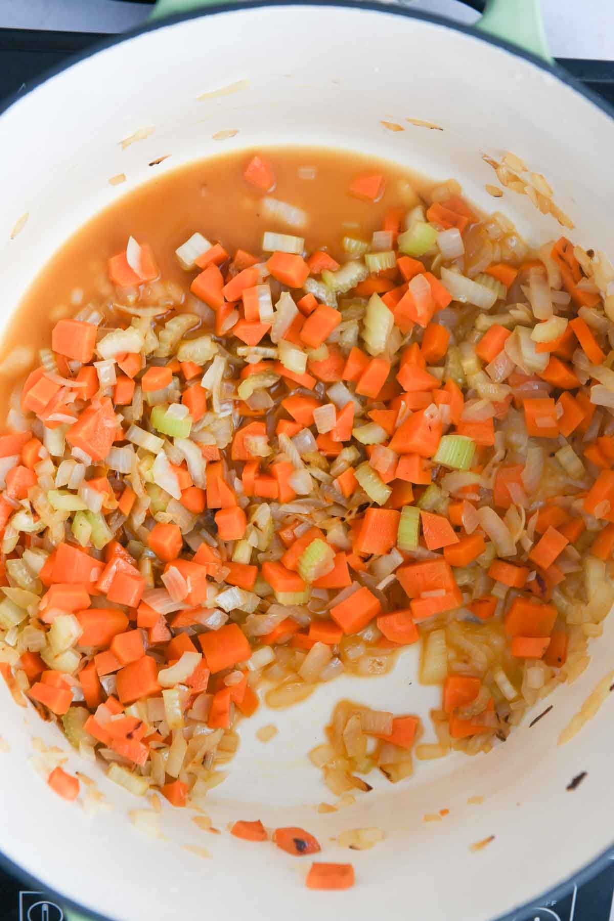 Sauteed onions, carrots, garlic, and celery in a white pot.
